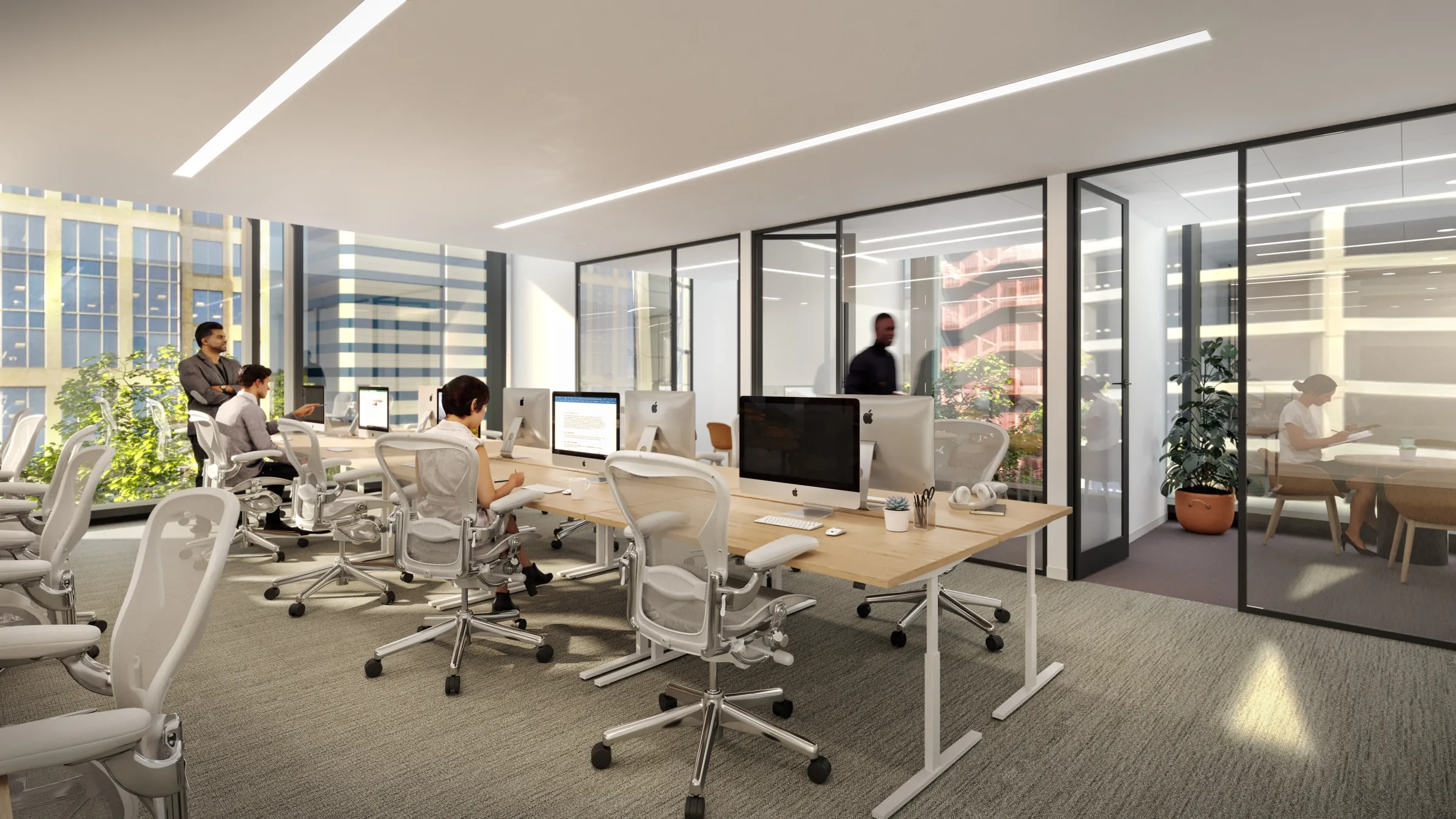 An open-plan office: desks with monitors and mesh chairs, glass-walled rooms beyond, and daylight from a full-height window.
