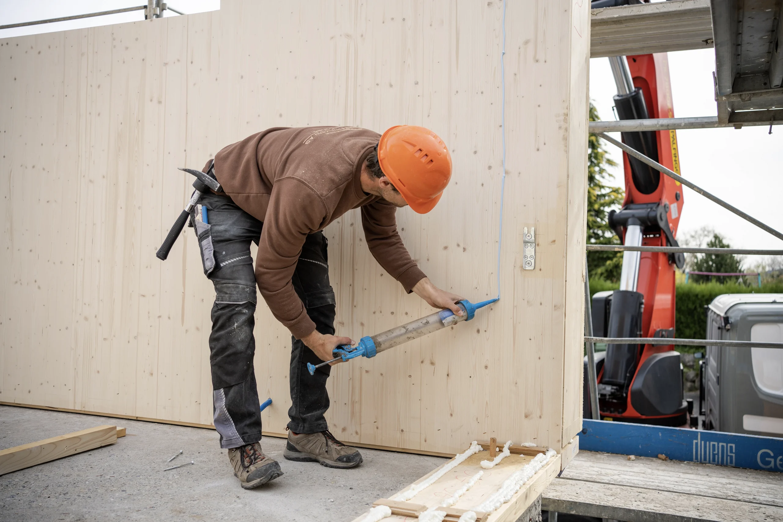 Riesen Holzbau AG carpenter in brown workwear and an orange helmet sealing the joint of a timber wall panel